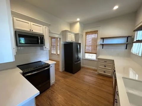 Clean modern kitchen with white cabinets, black appliances, and wooden flooring.
