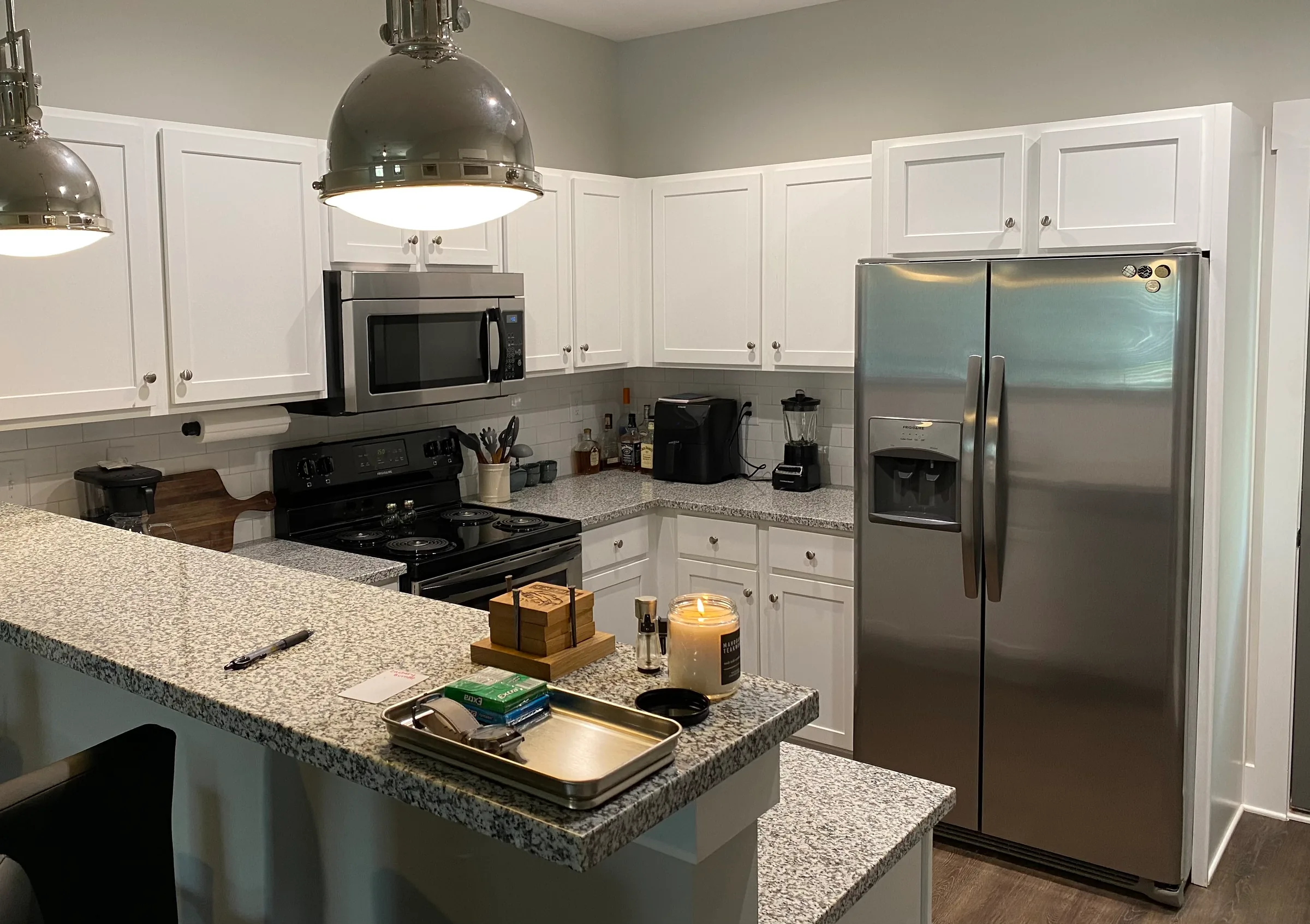 Modern kitchen with white cabinets, stainless steel appliances, granite countertops, and industrial pendant lighting.