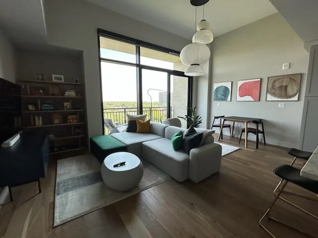 Modern living room with gray sectional sofa, white pendant lights, and large windows overlooking a balcony.