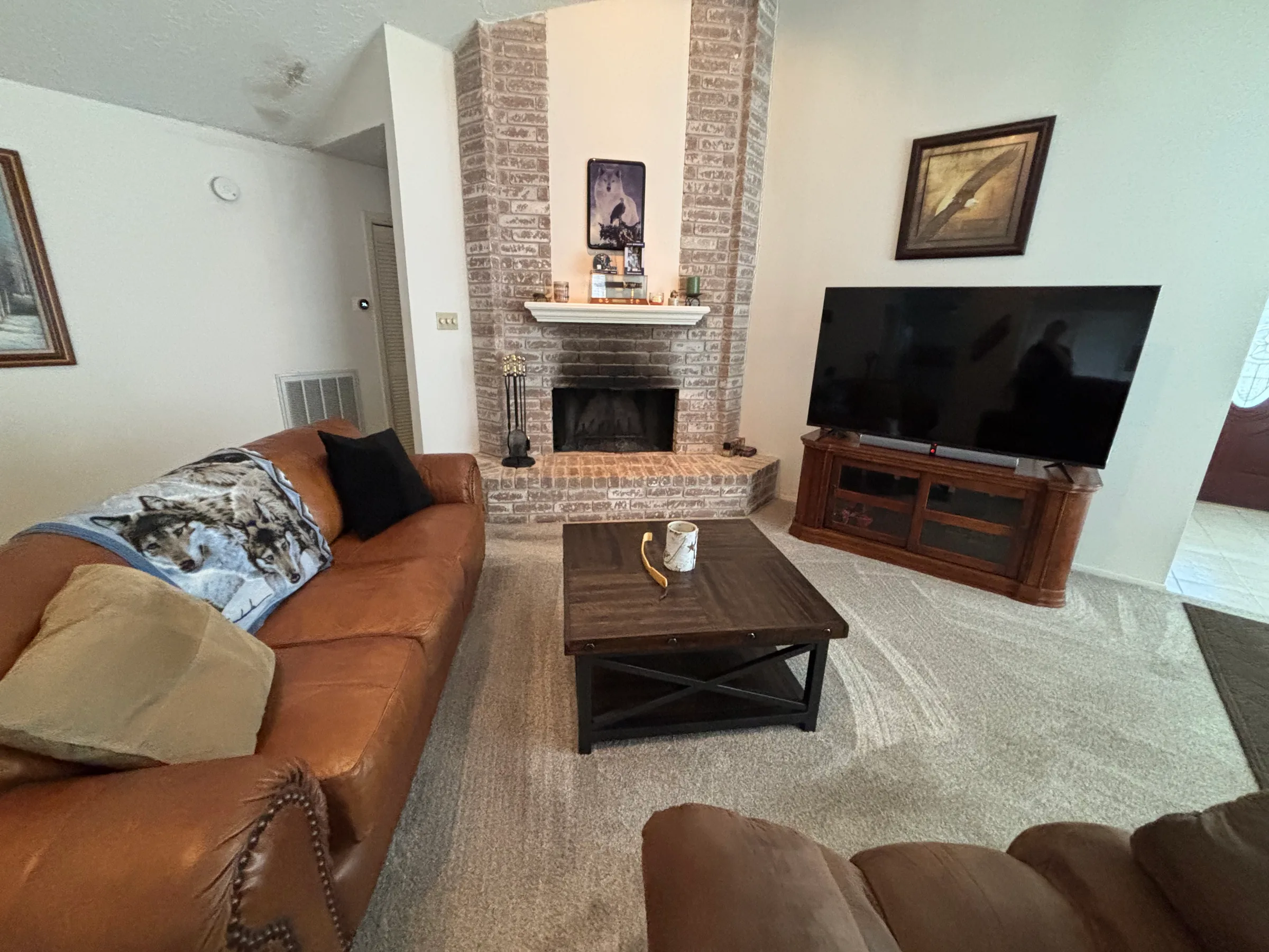 Spacious living room with brown leather sofa, fireplace, and flat-screen TV on wooden stand.